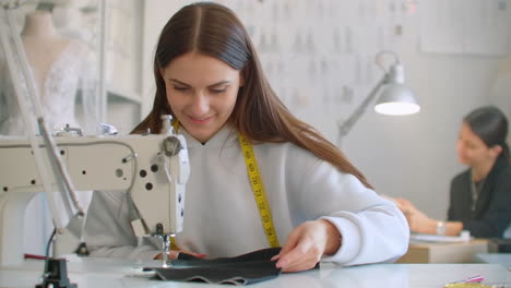Tailoring-of-clothes.-Seamstresses-at-work-in-workshop-sewing-clothes-on-sewing-machine.-Dressmakers-sews-clothes-in-atelier.-Two-women-seamstress.-Dressmaking-in-sewing-business.